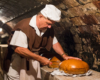 Piekarz przecinający pół metrowej wielkości chleby, w których wnętrzu są ukryte wcześniej peklowane golonki. Zapraszamy na niepowtarzalne smaki na wycieczkę jednodniową z Bieszczad na Węgry!